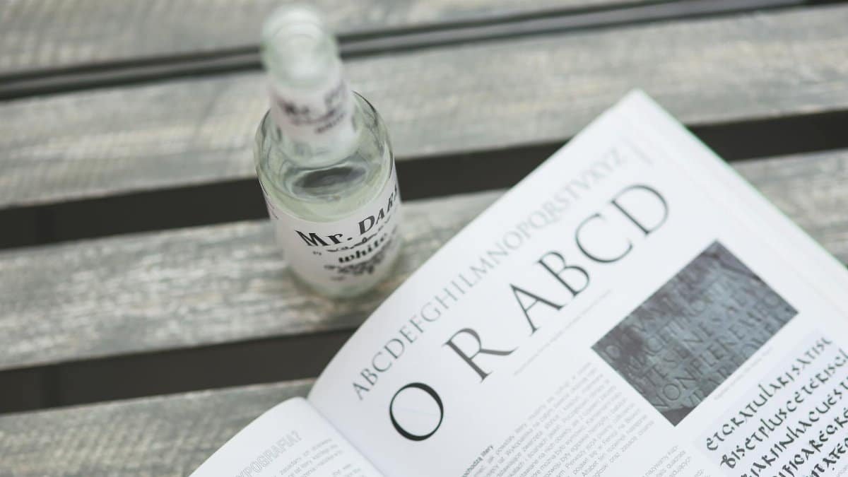 A bottle and an opened newspaper on a wooden table with focus on typography.