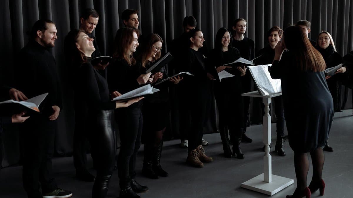A group of men and women singing with a conductor during choir practice.