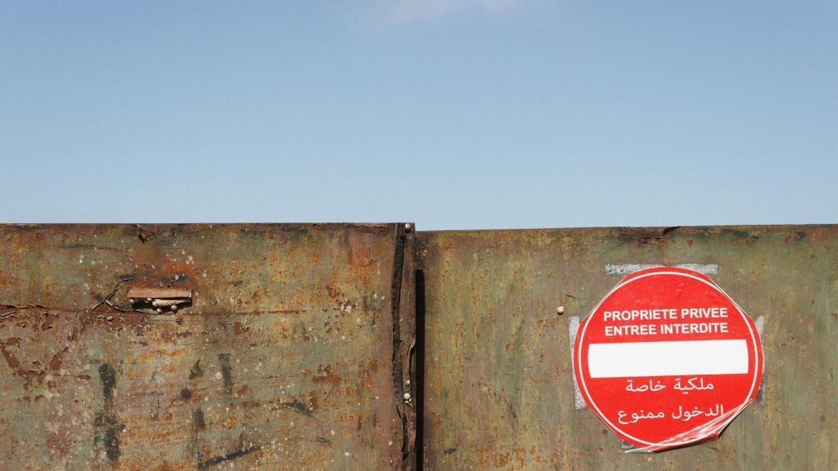 A rusty gate with a private property sign in French, outdoors on a clear day.