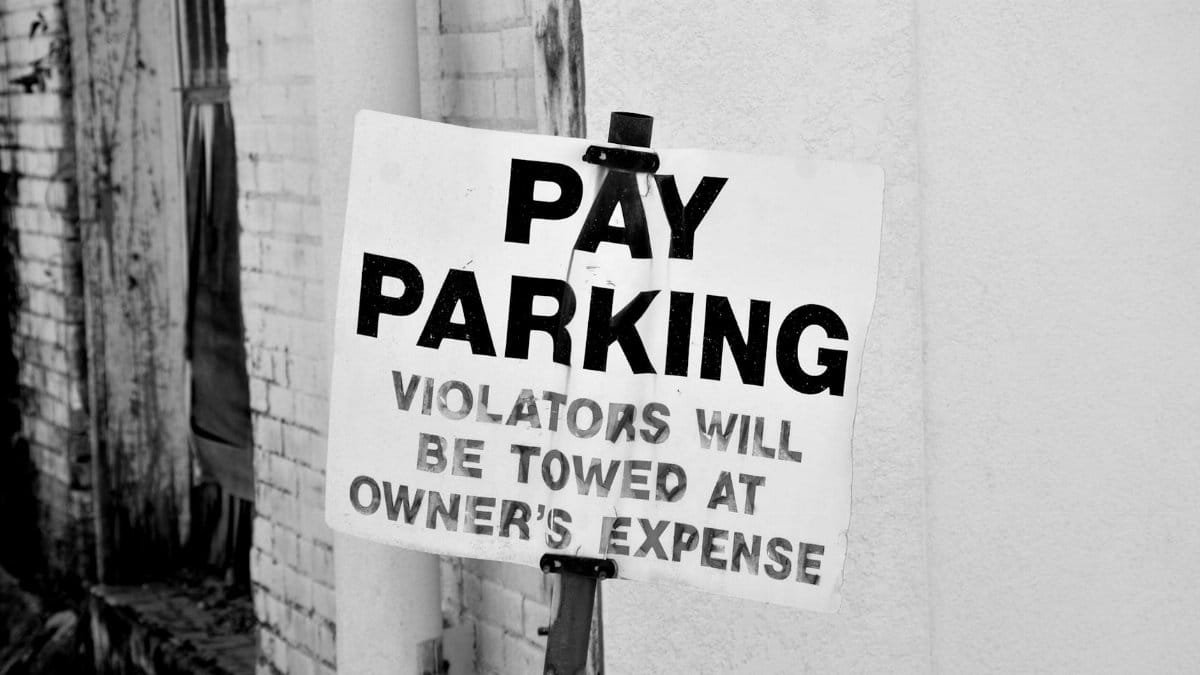 A black and white photo of a pay parking sign in downtown Tyler, Texas. Violators will be towed.
