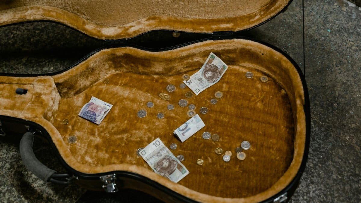 Open guitar case filled with various currencies and coins from street performance.