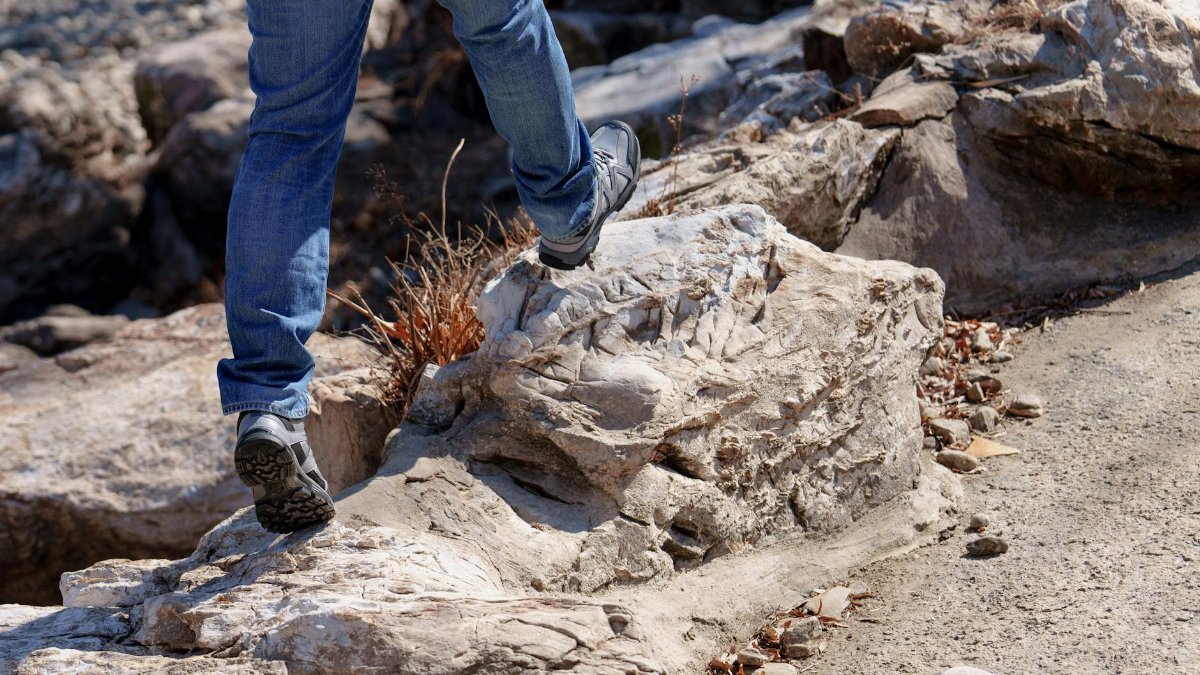 Lower view of a man in jeans hiking on a rocky path. Outdoor adventure scene.