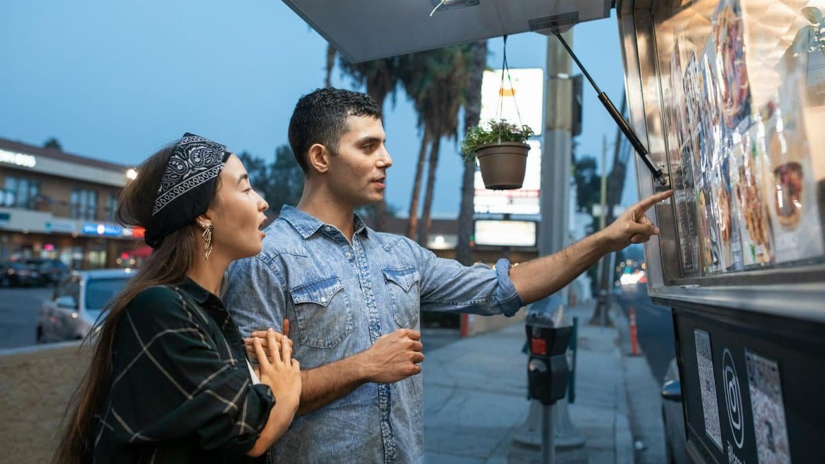 A man and woman exploring a local food truck menu during an evening out on the street.