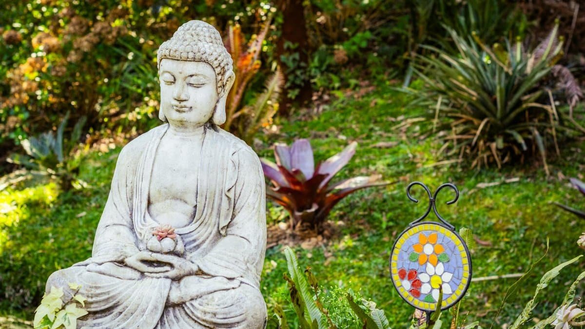A tranquil Buddha statue surrounded by lush greenery and vibrant plants in a serene garden.