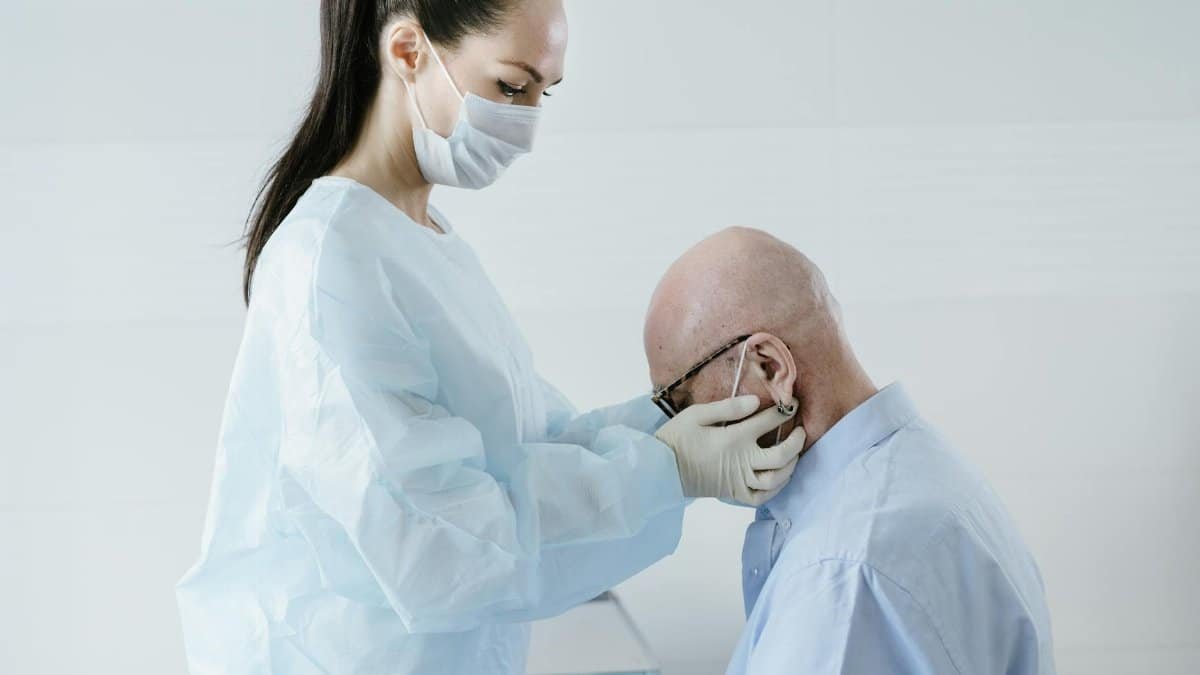 Masked doctor examines elderly patient in clinical setting, emphasizing health and hygiene.