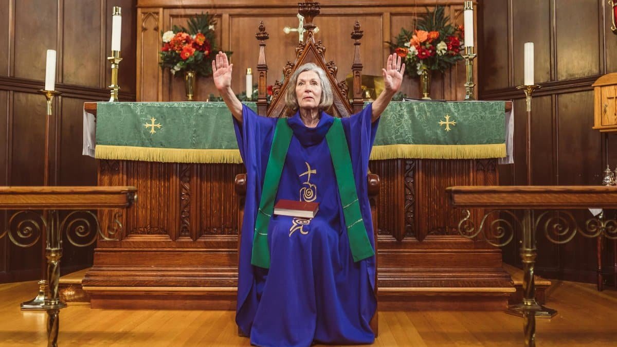 An elderly priest raises hands in prayer at the church altar, symbolizing faith and devotion.