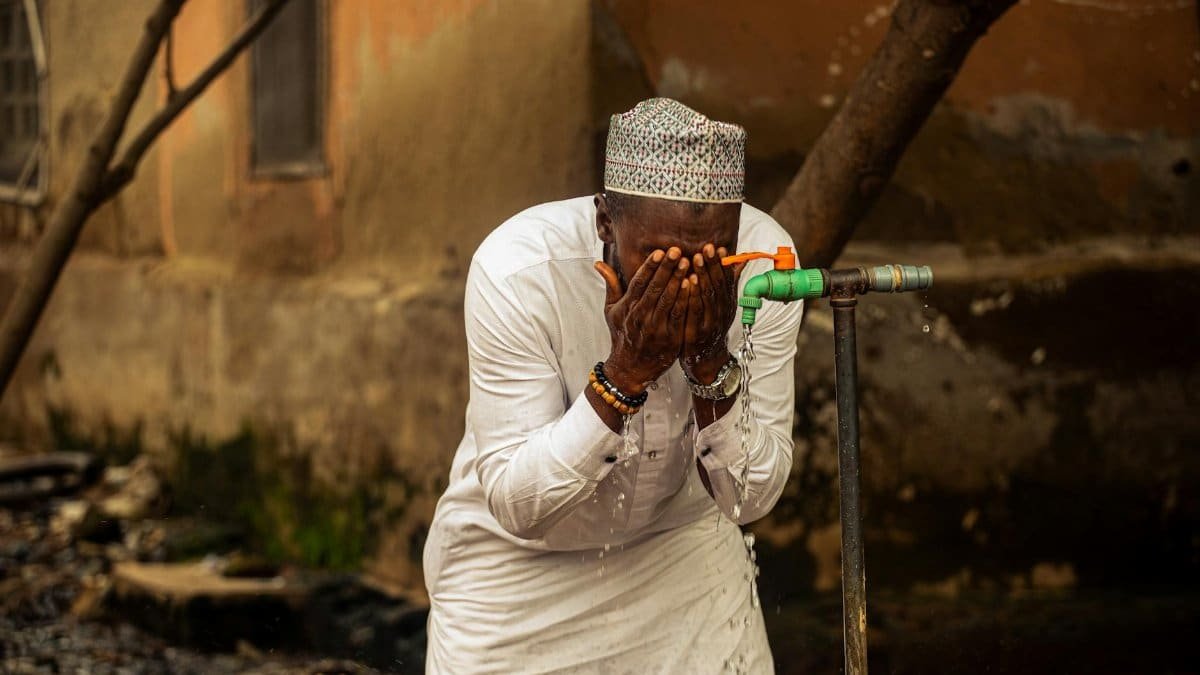 An adult man washing his face at an outdoor tap, showcasing daily life in Nigeria.