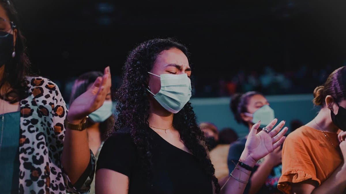 A group of adults wearing masks in a prayer setting, illustrating faith in pandemic times.