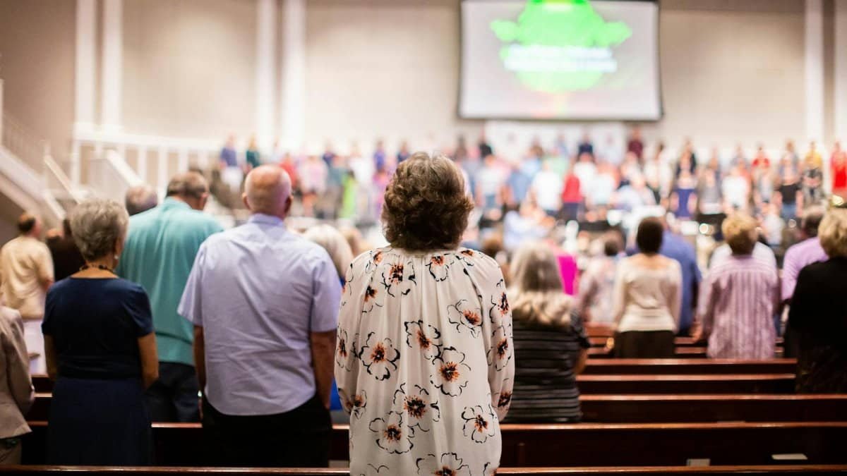 A congregation stands in reverence in a church, facing a stage with a worship team and projection screen.