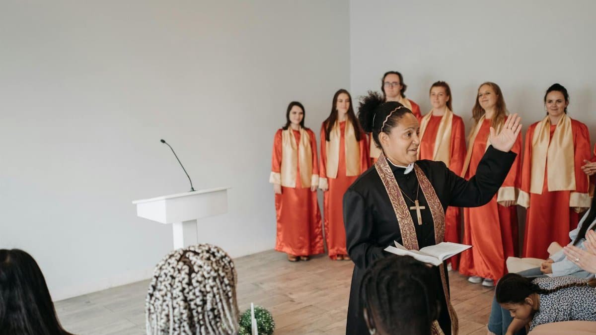A pastor leading a church ceremony with a choir in red robes in the background.