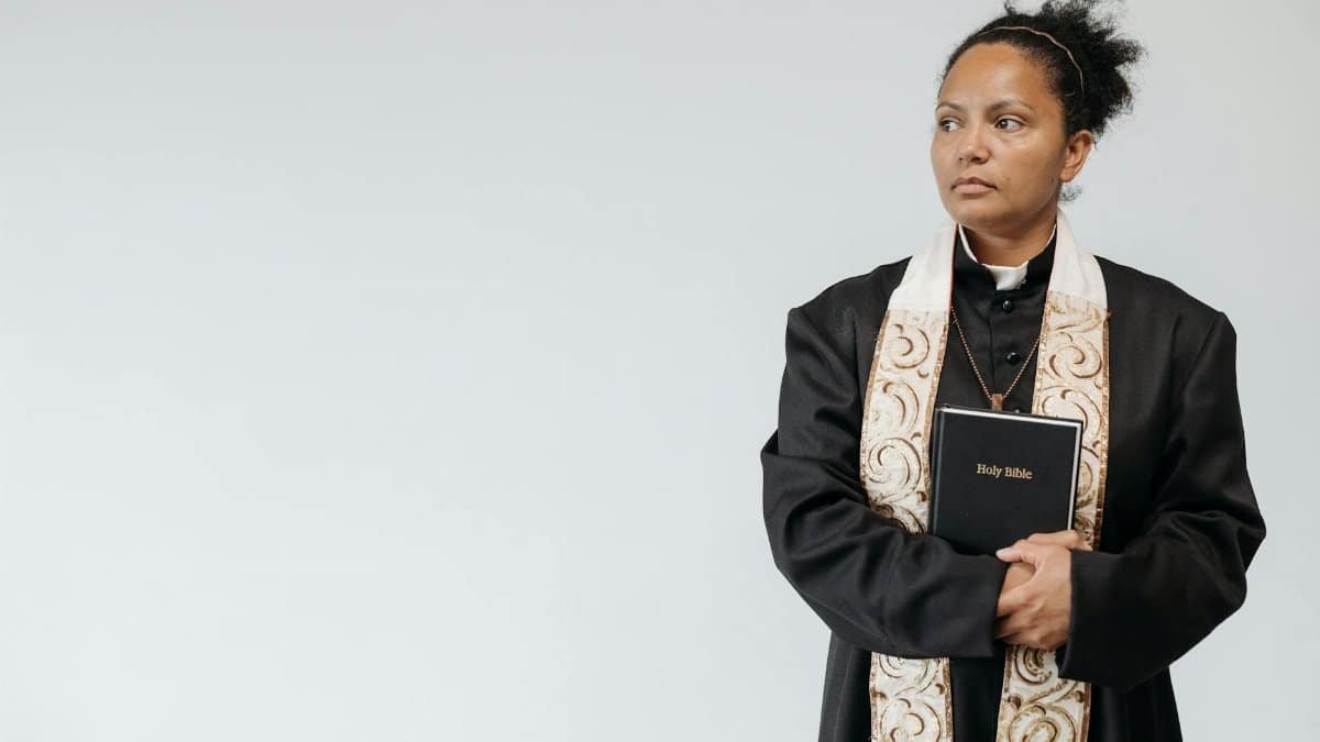 A female priest in religious attire holding a Holy Bible, symbolizing faith and spirituality.