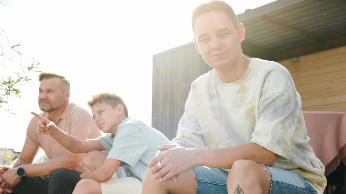 A father and two sons sitting outdoors, enjoying a sunny summer day together.