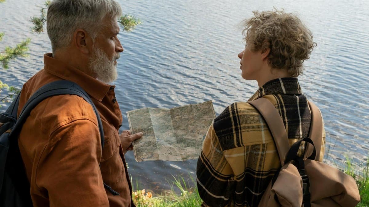Grandfather and grandson studying a map by a serene lake, enjoying family hiking time.