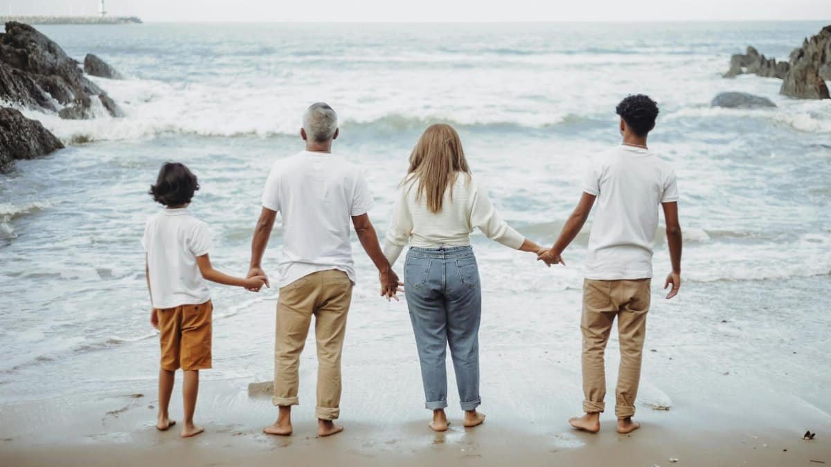 A family of four holds hands while facing the ocean, enjoying a peaceful day at the beach.