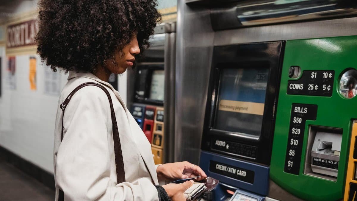 A woman uses a ticket machine in a subway station, handling her wallet and paying for transit.