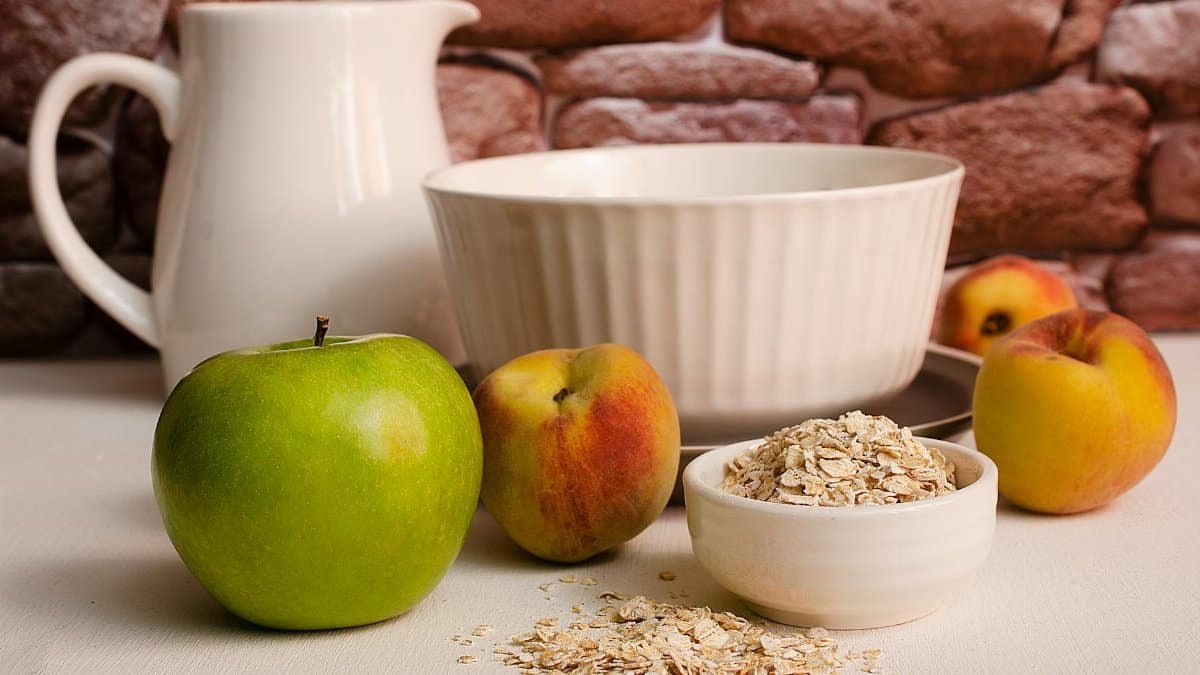 A close-up of a healthy breakfast arrangement featuring green apples, peaches, and oats in a rustic kitchen.