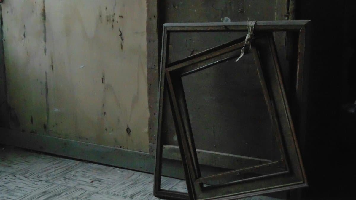Old wooden painting frames leaning against a faded wall in an abandoned room.