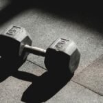 A single 40 lb dumbbell rests on the gym floor, highlighted by light and shadow play.