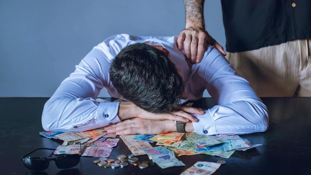 Depressed man surrounded by Argentine pesos represents financial stress and burnout.