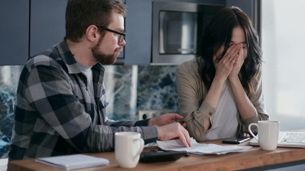Young couple stresses over bills at home, illustrating financial struggle.