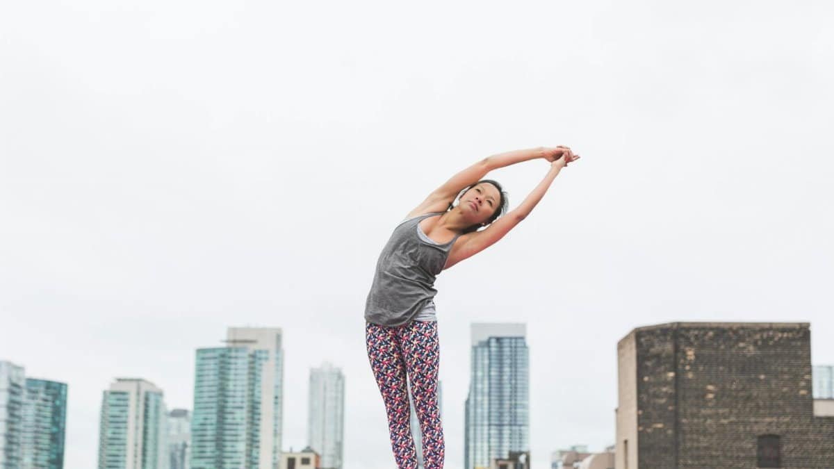 A woman practices yoga on a rooftop with a city skyline in the background, embodying urban fitness.
