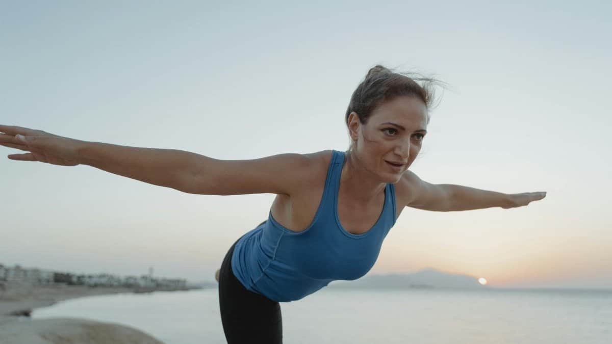 Woman in a yoga pose on a beach during sunrise, focusing on balance and concentration.