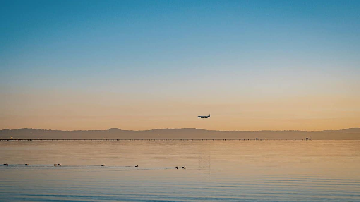 A serene view of an airplane flying over calm ocean waters at sunset, with warm tones and peaceful ambiance.