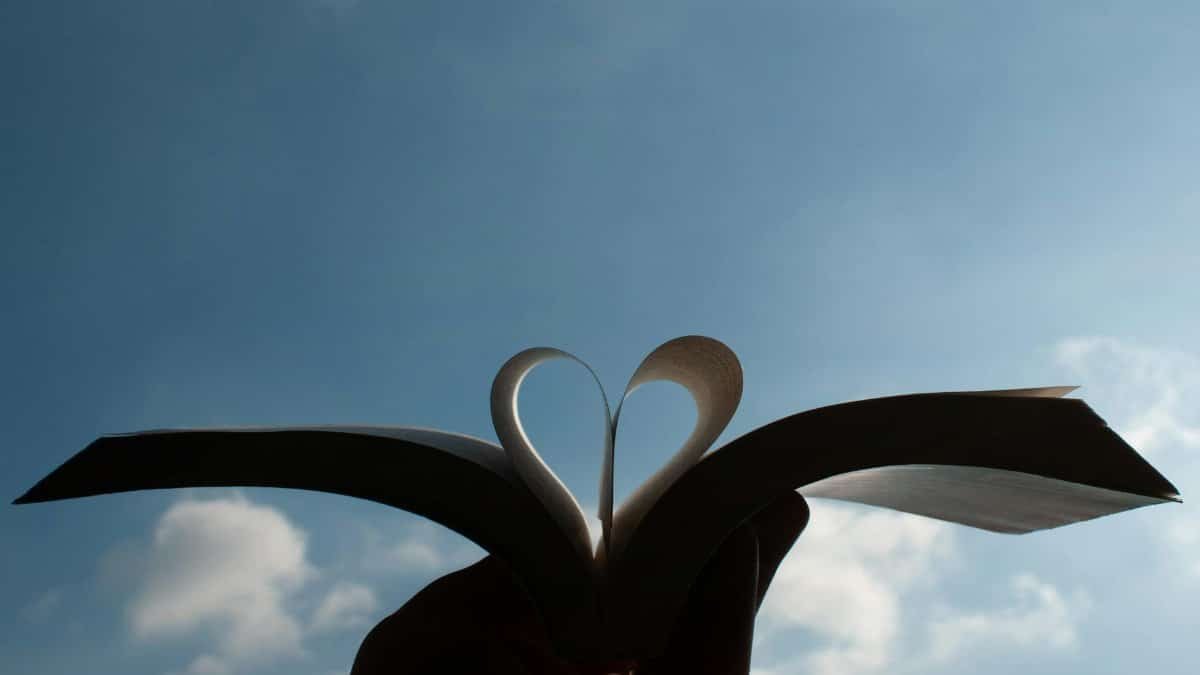 A heart shape formed by an open book's pages with a clear blue sky background in Milano, Italy.