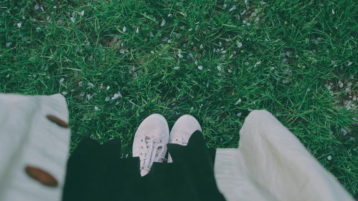 A top-down view of shoes and coat on grassy ground scattered with petals, capturing spring vibes.