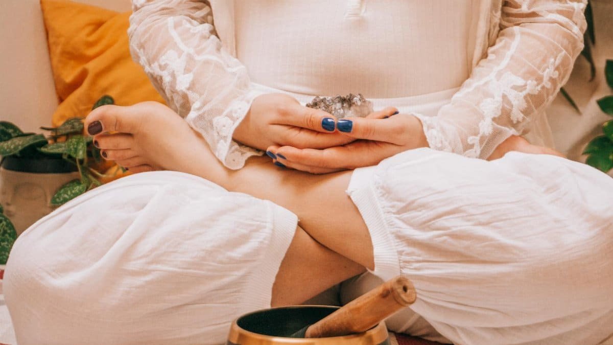 Woman in meditation holding crystal, seated in lotus position with a Tibetan singing bowl, promoting relaxation.