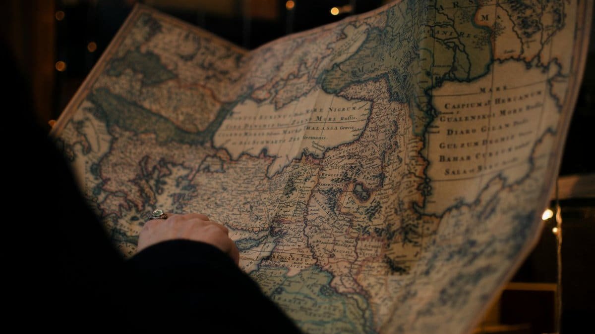 From behind anonymous person examining antique world map printed on large paper in blue colors in dark room