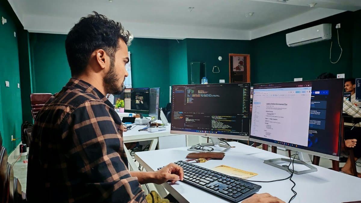 Software developer coding on dual monitors in a well-lit modern office, focused and engaged.