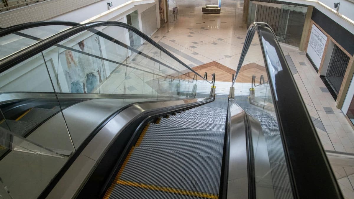 An escalator inside a deserted shopping mall with closed storefronts and empty spaces, capturing urban decay.