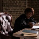 Black female judge in judicial robe writing at desk in an office setting, focusing on legal work.