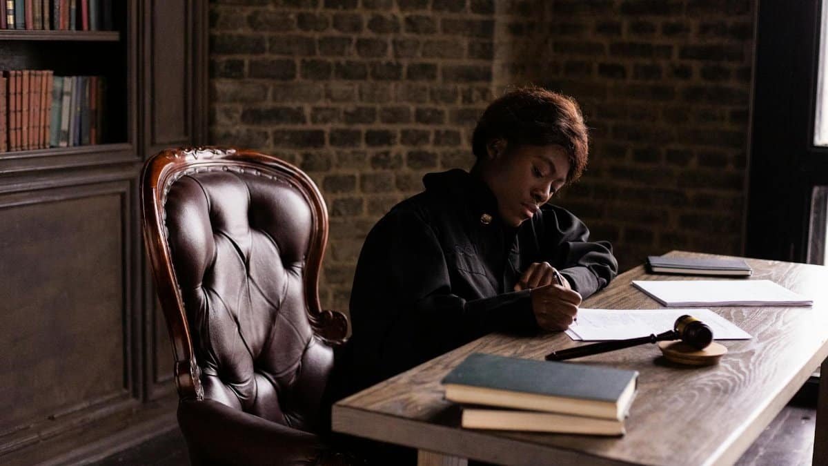 Black female judge in judicial robe writing at desk in an office setting, focusing on legal work.