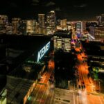 Drone view of asphalt roads between illuminated multistory buildings at night in Fort Lauderdale city