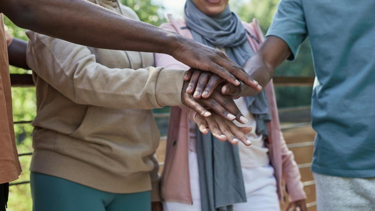A diverse group of friends stacking hands in a symbol of unity outdoors.