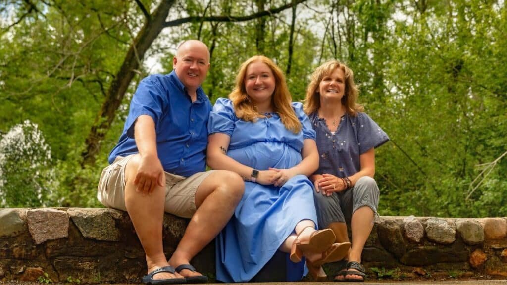 A joyful family of three sitting on a stone bench in a lush green outdoor setting.