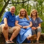 A joyful family of three sitting on a stone bench in a lush green outdoor setting.