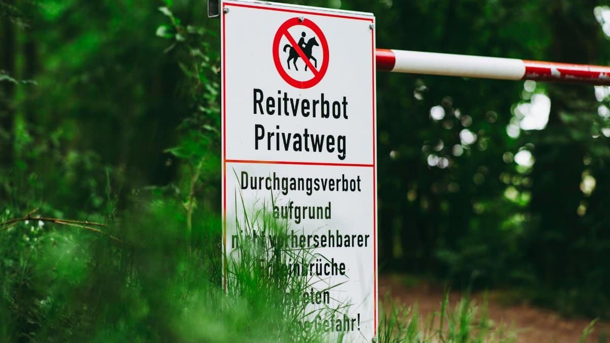 Close-up of a German sign prohibiting horse riding on a private road in a lush forest setting.