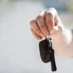 Close-up of a hand handing over car keys, signifying purchase or rental.
