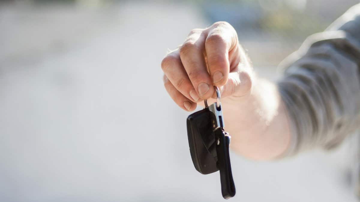 Close-up of a hand handing over car keys, signifying purchase or rental.