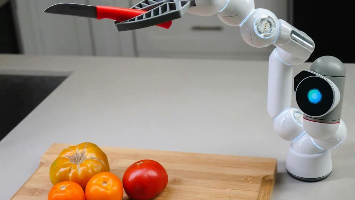 A futuristic robotic arm with a knife preparing colorful tomatoes in a modern kitchen.
