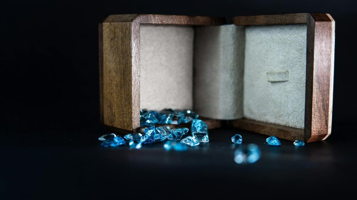 Wooden jewelry box displaying scattered blue gems, symbolizing elegance and luxury.