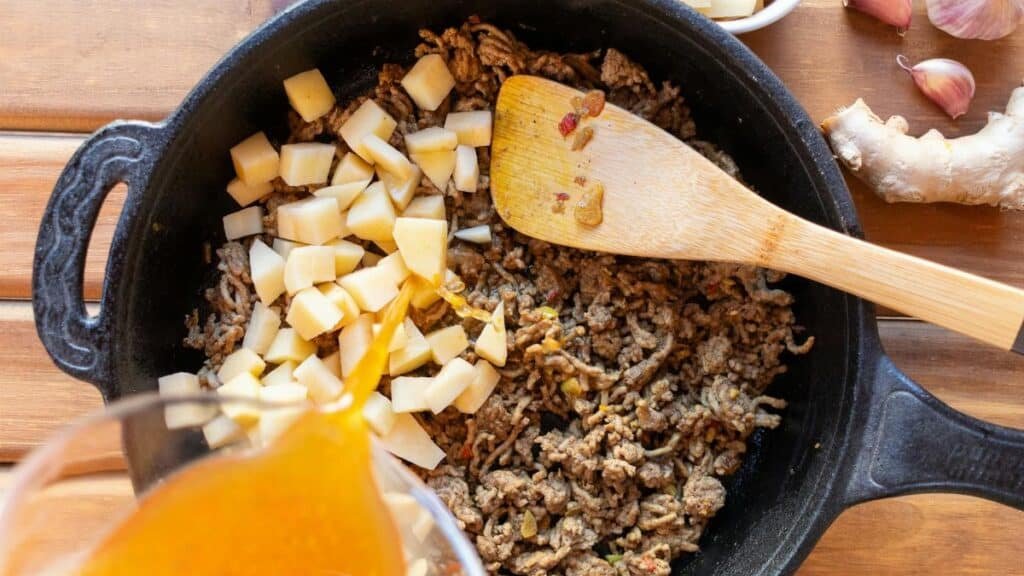 Ground beef and potatoes cooked in a skillet with broth poured in for a hearty meal.