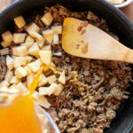 Ground beef and potatoes cooked in a skillet with broth poured in for a hearty meal.