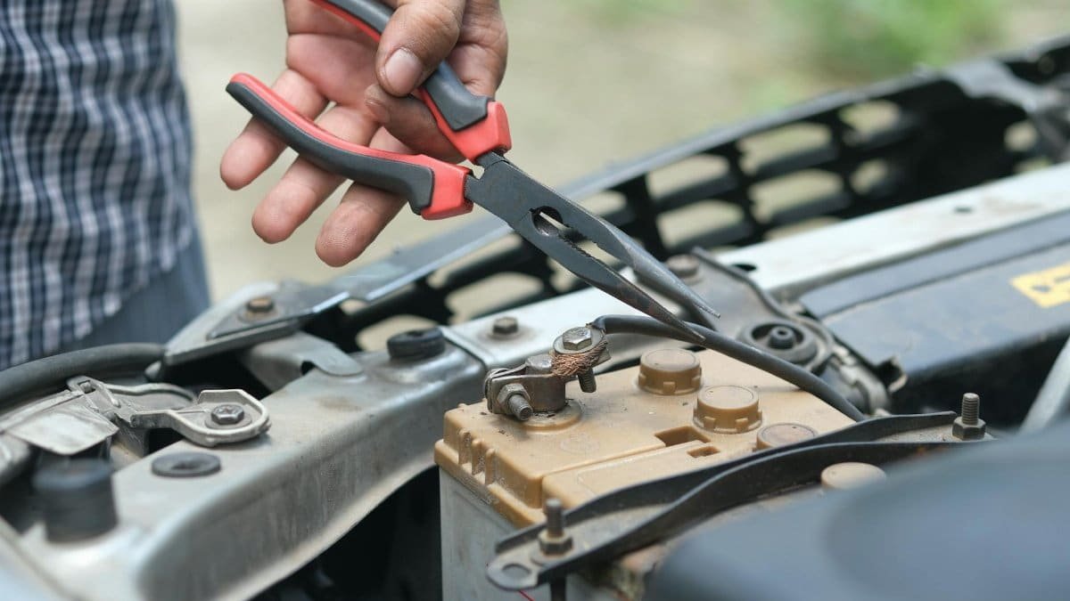 Person using pliers to check a car battery in an outdoor setting.
