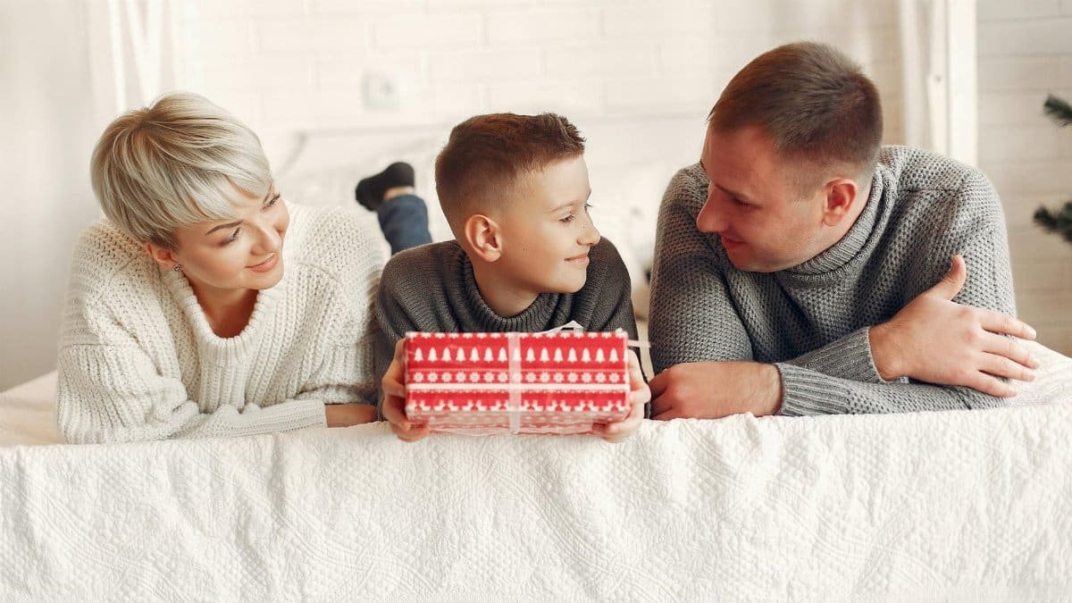 Smiling family enjoying quality time while unwrapping a gift on a cozy white bed.