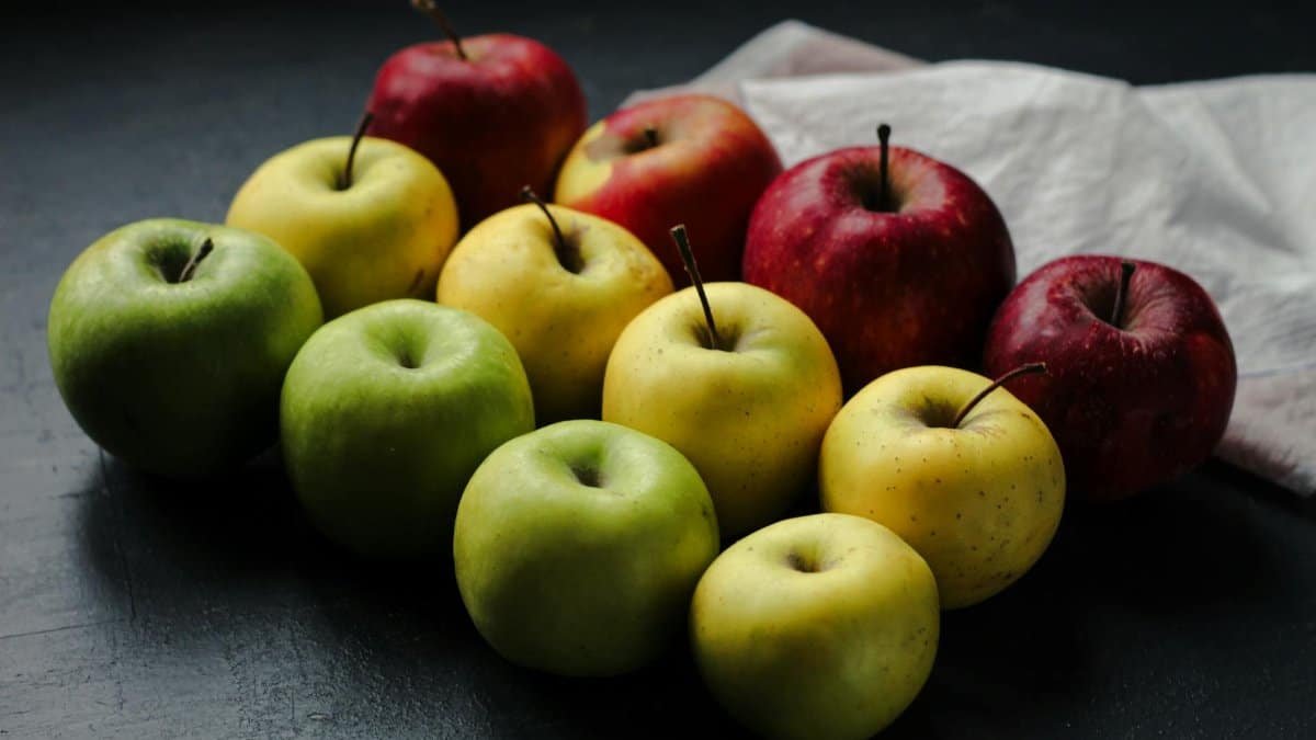 Colorful display of red, green, and yellow apples on a dark table.
