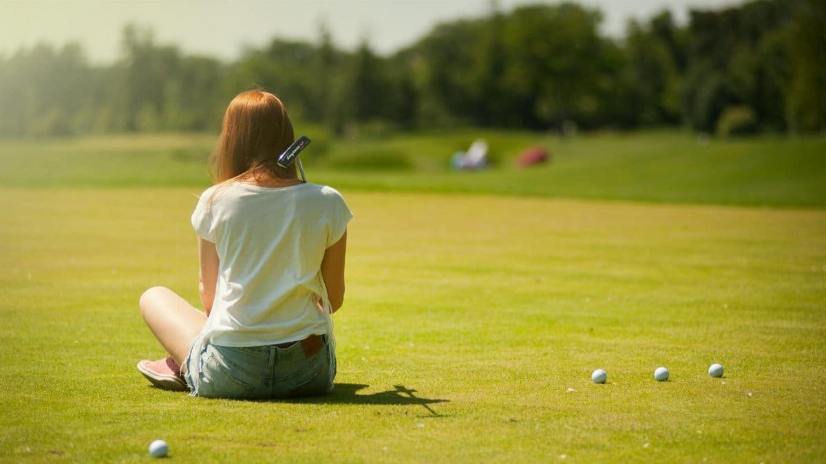 A young woman sitting on a golf course in summer, enjoying leisure time outdoors.